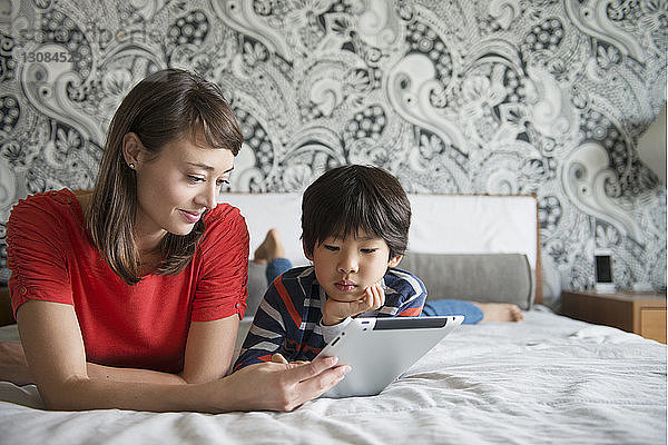 Mutter und Sohn liegen auf dem Bett und benutzen ein digitales Tablett