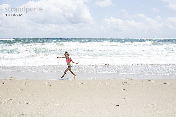 Verspieltes Mädchen rennt am Strand gegen bewölkten Himmel