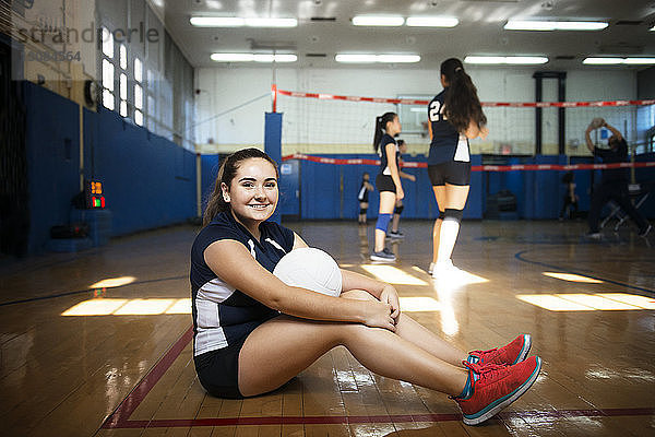Porträt eines Mädchens  das Volleyball hält und auf dem Boden sitzt