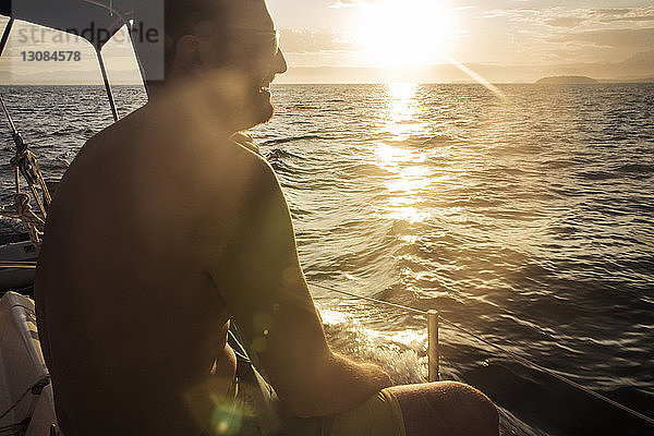Glücklicher Mann sitzt bei Sonnenuntergang im Boot auf See