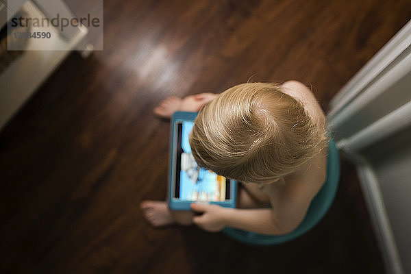 Hochwinkelaufnahme eines Jungen mit einem Tablet-Computer  der zu Hause auf dem Töpfchen sitzt