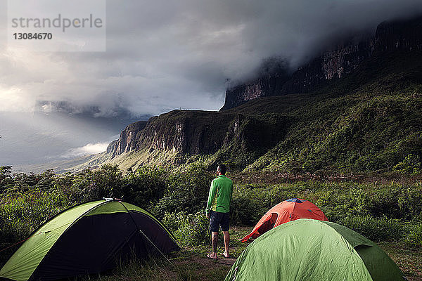 Rückansicht eines Mannes  der auf einem Campingplatz auf einem grünen Berg steht