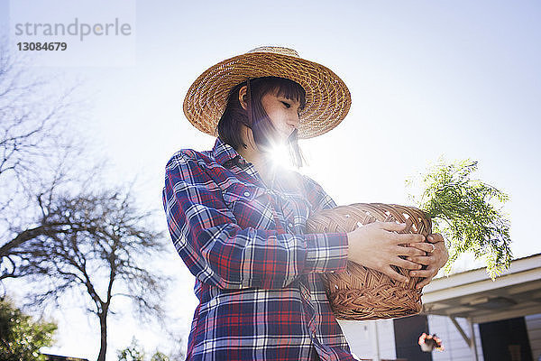 Junge Bäuerin trägt Korb bei sonnigem Wetter im Betrieb