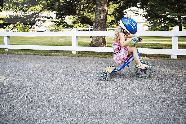 Seitenansicht eines Mädchens auf einem Dreirad mit Helm auf der Straße