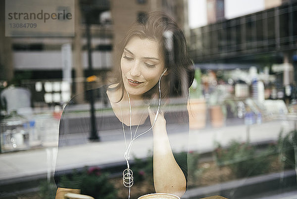 Frau benutzt Mobiltelefon  während sie im Café sitzt  durch Fenster gesehen