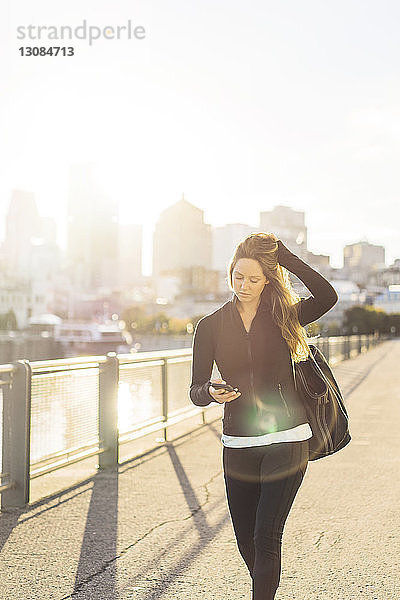 Frau benutzt Smartphone beim Spaziergang in der Stadt an einem sonnigen Tag