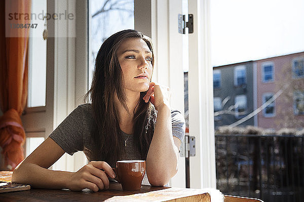 Nachdenkliche Frau mit Kaffeetasse auf dem Tisch zu Hause