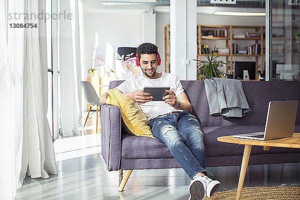 Glücklicher Geschäftsmann mit Tablet-Computer während er sich im Büro auf dem Sofa entspannt