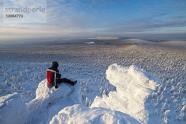 Wanderer betrachtet Aussicht  während er im schneebedeckten Berg gegen den Himmel sitzt