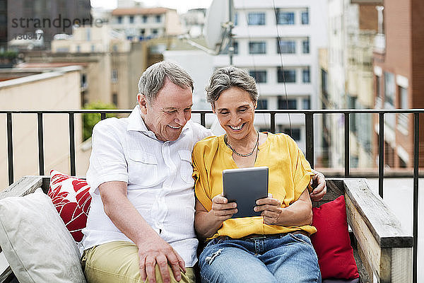 Fröhliches älteres Ehepaar benutzt Tablet-Computer  während es auf einer Bank auf der Terrasse sitzt