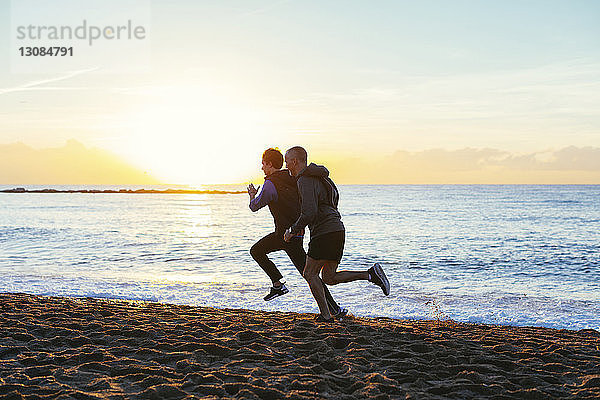 Vater und Sohn joggen in voller Länge an der Küste am Strand gegen den Himmel