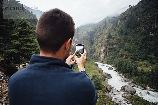 Rückansicht eines männlichen Wanderers beim Fotografieren eines Flusses inmitten der Berge im Sagarmatha-Nationalpark