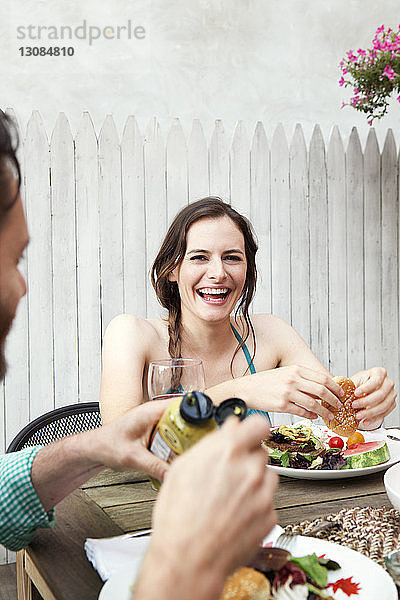 Glückliche Frau mit Freund beim Essen  während sie im Hof am Tisch sitzt