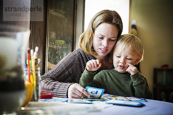 Mutter zeigt dem Sohn Karten  während sie am Tisch sitzt