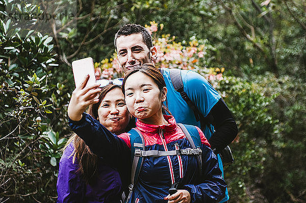 Fröhliche Freunde  die im Wald stehen und Selfie nehmen