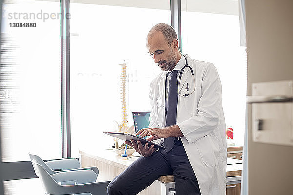 Arzt benutzt Tablet-Computer  während er im Krankenhaus am Schreibtisch sitzt