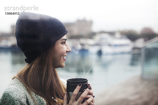 Seitenansicht einer glücklichen Frau  die im Hafen Kaffee trinkt