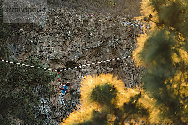 Mann hängt bei Sonnenuntergang an Slackline am Berg