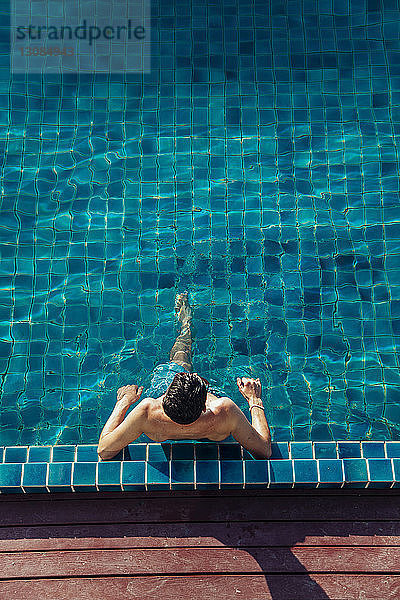 Hochwinkelansicht eines Mannes ohne Hemd  der sich im Schwimmbad eines Touristenortes entspannt