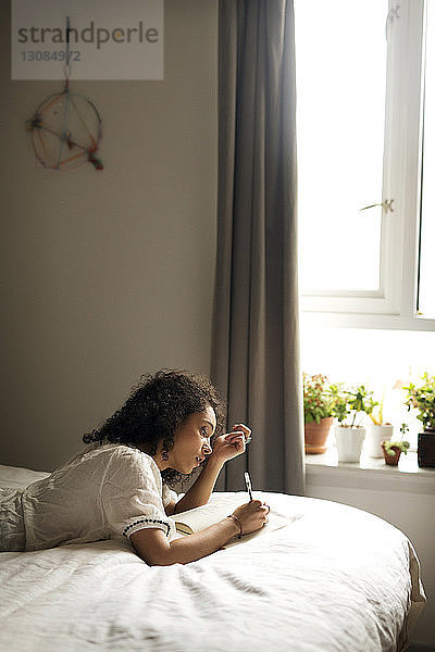Seitenansicht einer Frau  die auf ein Buch schreibt  während sie sich im Schlafzimmer entspannt