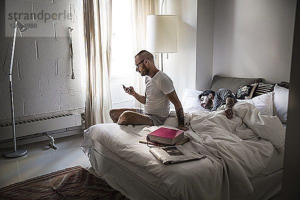 Schwuler Mann benutzt Telefon  während der Partner im Bett schläft