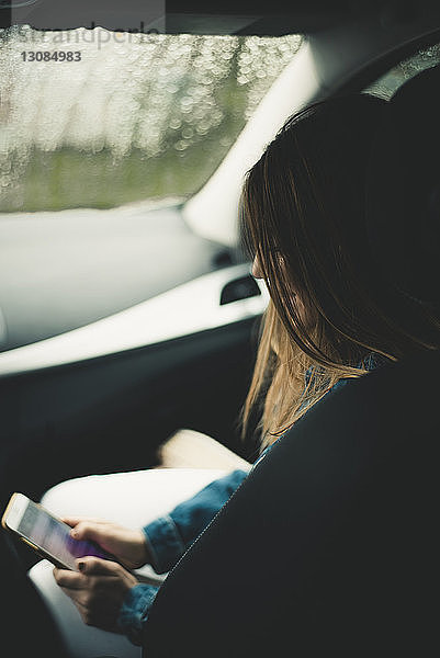 Seitenansicht einer Frau  die während der Fahrt im Auto ein Mobiltelefon benutzt