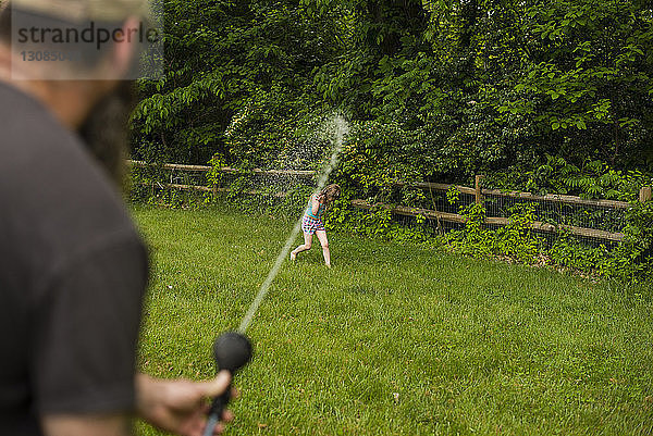 Verspielter Vater bespritzt ein Mädchen im Garten mit einem Schlauch mit Wasser