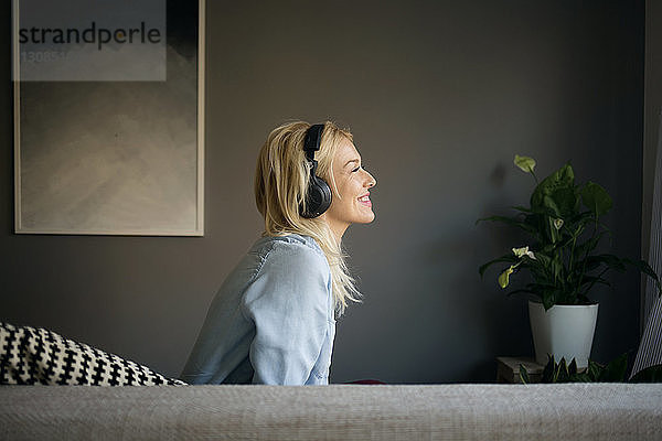 Seitenansicht einer glücklichen Frau  die Musik hört  während sie zu Hause auf dem Sofa sitzt