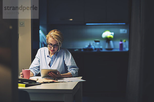 Geschäftsfrau  die einen Tablet-Computer benutzt  während sie im Heimbüro am Schreibtisch sitzt