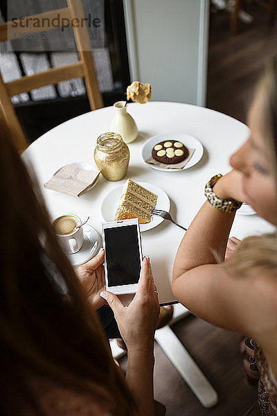 Draufsicht auf Frauen  die ein Smartphone am Café-Tisch benutzen