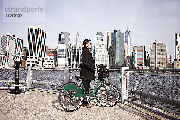 Seitenansicht eines Geschäftsmannes mit Fahrrad  der vom Aussichtspunkt aus die Stadt genießt