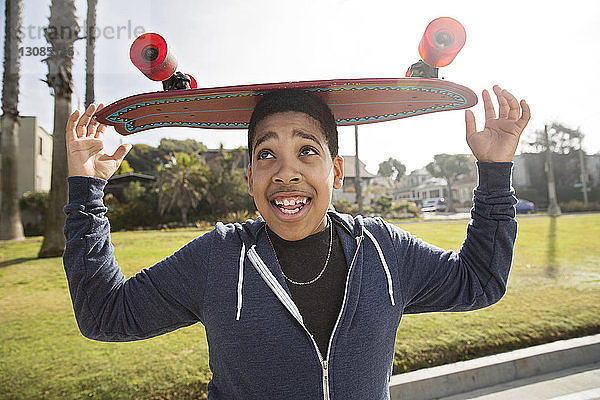 Verspielter Teenager  der im Park Skateboard auf dem Kopf balanciert