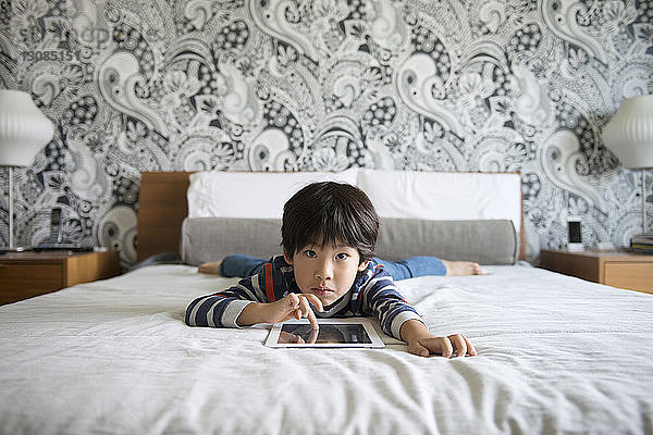 Porträt eines Jungen  der auf dem Bett liegt und ein digitales Tablett benutzt