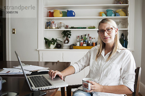 Porträt einer selbstbewussten Frau  die zu Hause einen Laptop benutzt