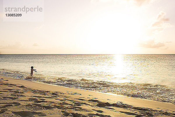 Junge spielt am Strand gegen den Himmel an einem sonnigen Tag