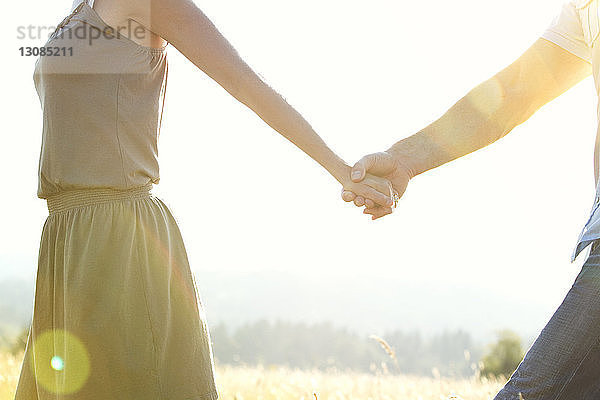 Ausgeschnittenes Bild eines Mannes  der die Hand seiner Freundin hält  während er auf dem Feld geht