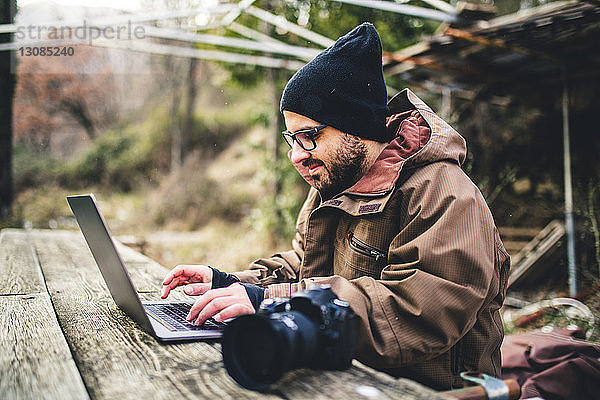 Seitenansicht eines männlichen Wanderers mit Laptop-Computer und Kamera auf einem Tisch im Wald