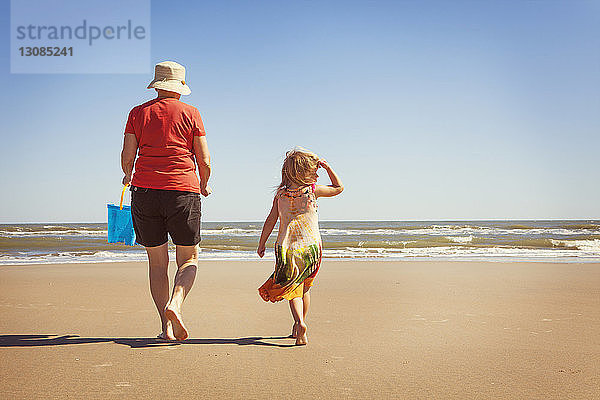 Rückansicht von Enkelin und Großmutter  die am Strand auf Sand laufen