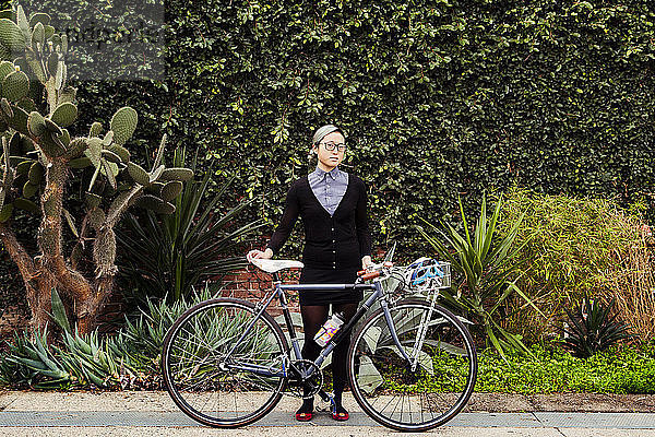 Porträt einer Geschäftsfrau  die mit dem Fahrrad vor Pflanzen steht