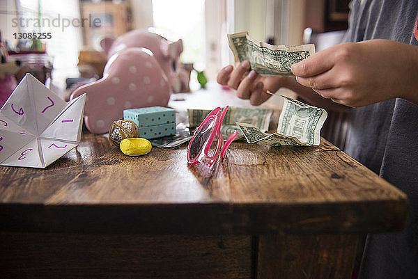 Mittendrin ein Mädchen  das Geld zählt  während es zu Hause an einem Holztisch steht