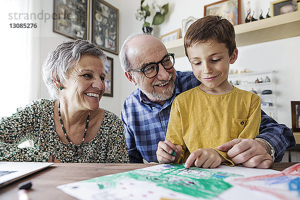 Glückliche Großeltern schauen zu Hause dem Enkel beim Zeichnen zu