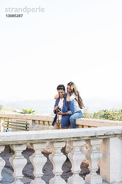 Glückliches Paar sieht sich Fotos auf der Terrasse bei klarem Himmel an