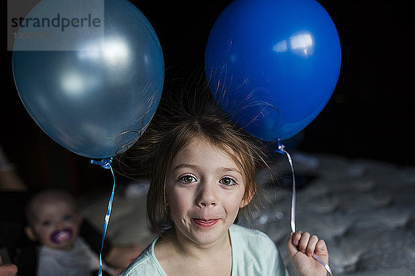 Porträt eines zu Hause stehenden Mädchens  das Ballons hält