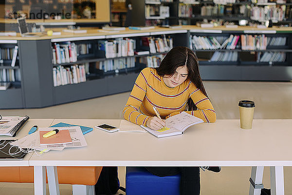 Schrägansicht einer Frau  die am Tisch sitzend in der Bibliothek schreibt