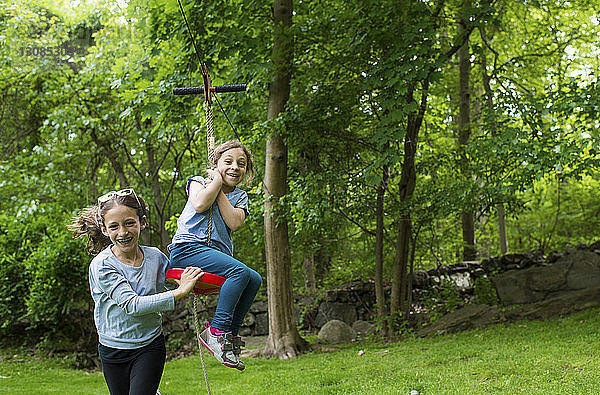 Glückliche Schwestern spielen mit der Seilrutsche im Park