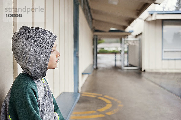 Nachdenklicher Junge sitzt auf Bank am Fussweg