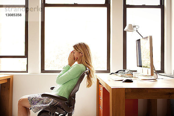 Müde Geschäftsfrau sitzt am Büroschreibtisch am Fenster