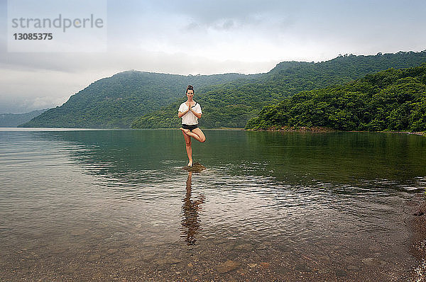 Frau in voller Länge beim Yoga auf einem Felsen inmitten eines Bergsees