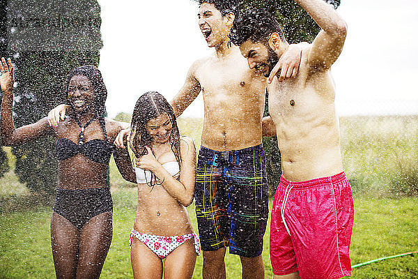 Fröhliche Freunde in Badebekleidung genießen Wasserspray im Hof