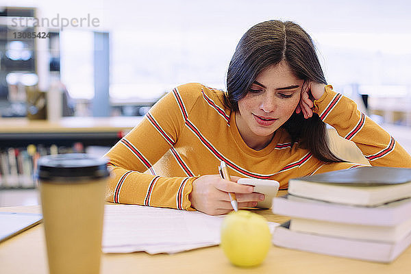 Frau benutzt Mobiltelefon während des Studiums in der Bibliothek